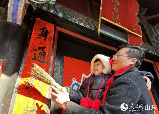 春節(jié)前，孔子后裔在孔府重光門前貼春聯(lián)。 人民網(wǎng) 喬姝攝